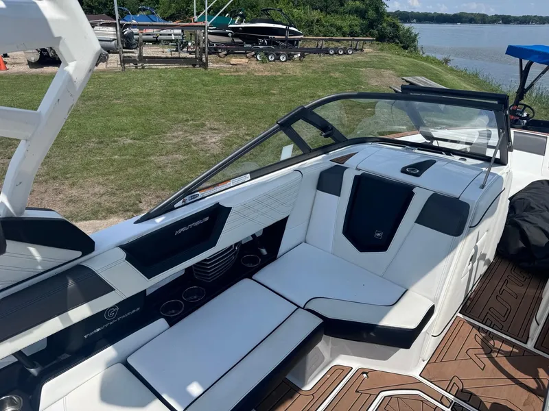 Slide: The Image of 2018 Nautique G23 boat interior with white seating and brown flooring by a lakeside. - 8