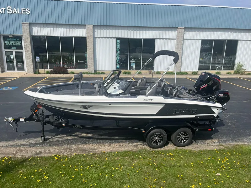 Slide: The Image of 2025 Lund 202 Pro-V GL boat on trailer, parked outside a sales building. - 2