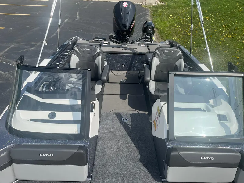 Slide: The Image of 2025 Lund 202 Pro-V GL boat interior with seating and windshield, parked on pavement. - 24