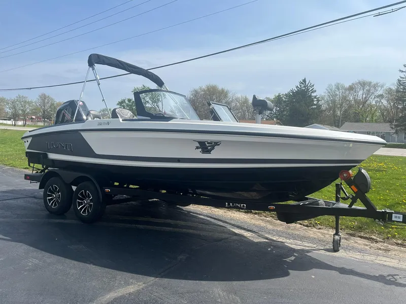 Slide: The Image of 2025 Lund 202 Pro-V GL boat on trailer, parked outdoors on a sunny day. - 5