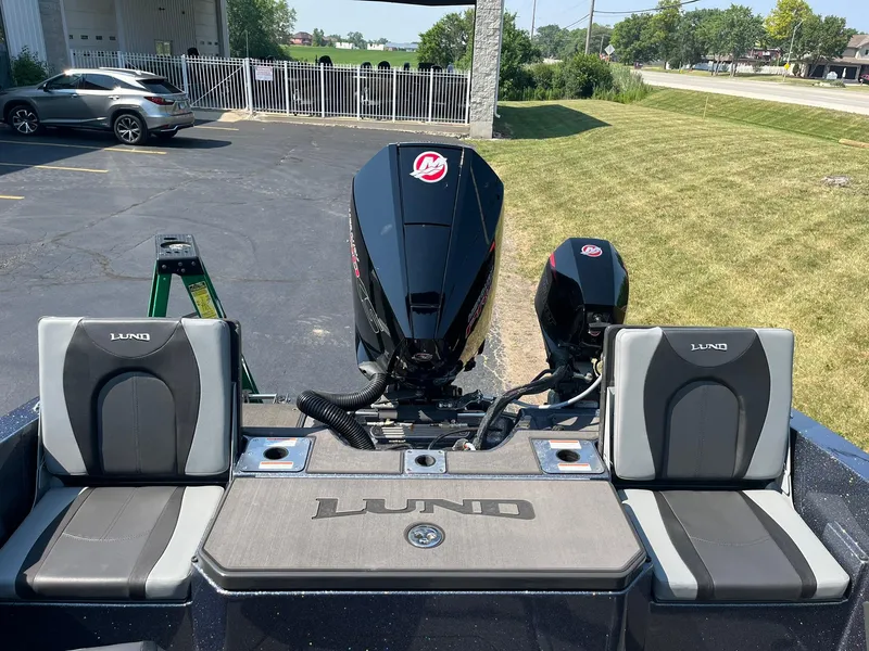 Slide: The Image of 2025 Lund 202 Pro-V GL boat with dual engines and cushioned seating, parked outdoors. - 10