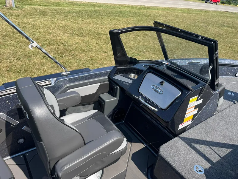 Slide: The Image of 2025 Lund 202 Pro-V GL boat interior with seating and dashboard, parked on grass. - 16