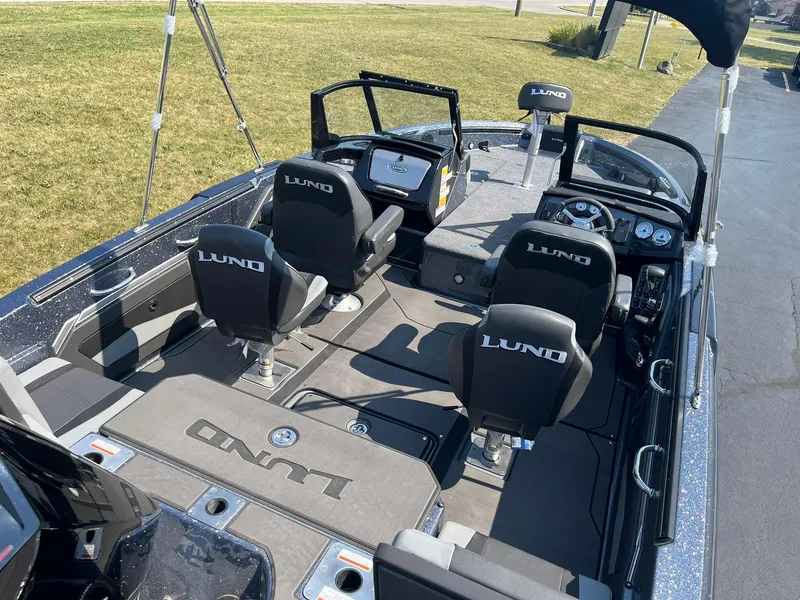 Slide: The Image of 2025 Lund 202 Pro-V GL boat interior with seating and dashboard, parked on grass. - 6
