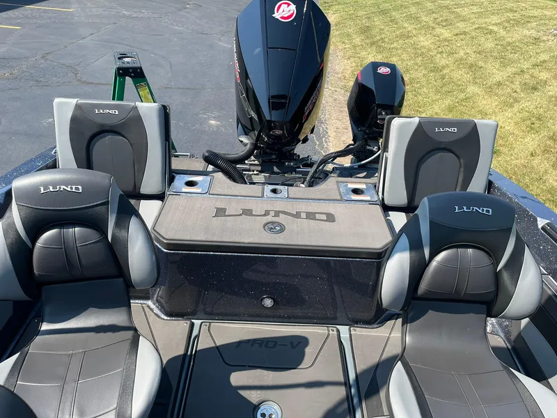 Slide: The Image of 2025 Lund 202 Pro-V GL boat interior with branded seats and motor, parked on pavement. - 9