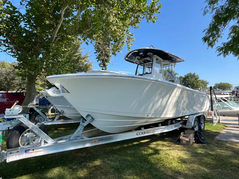 The Image of 2025 Cobia 265 CC boat on trailer under trees, sunny day. - 0