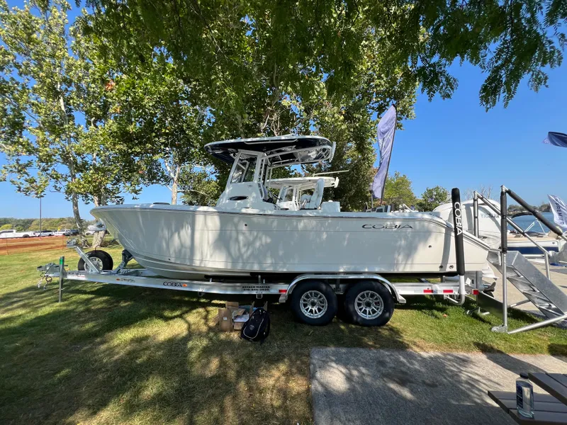 Slide: The Image of 2025 Cobia 265 CC boat on trailer under trees, sunny day. - 1