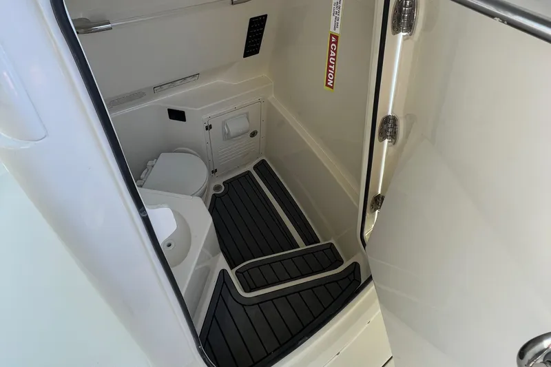 Slide: The Image of 2025 Cobia 265 CC boat interior with compact bathroom and caution sign. - 12