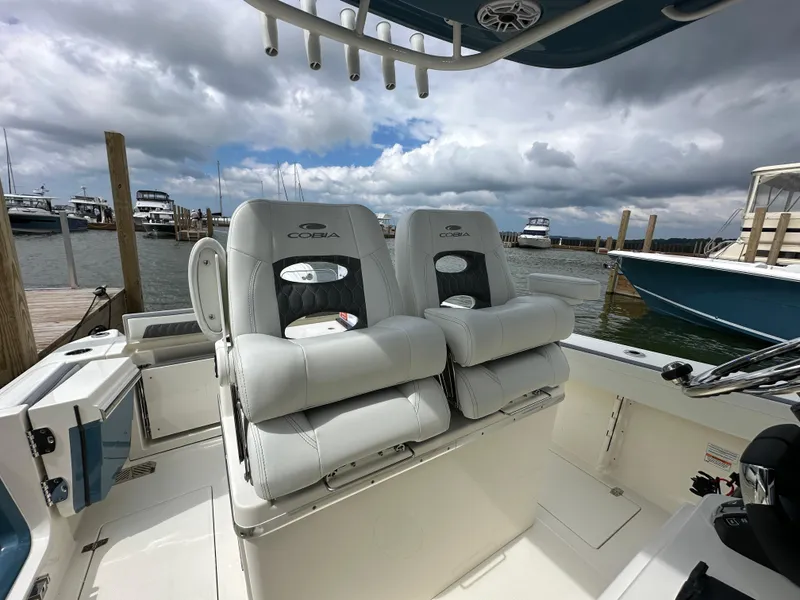 Slide: The Image of 2025 Cobia 265 CC boat interior with plush seating at a marina. - 7