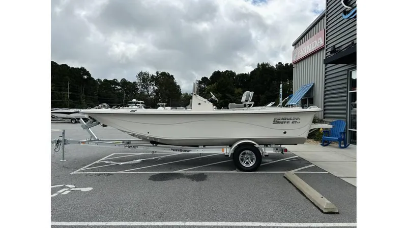 Slide: The Image of 2025 Carolina Skiff 21 LS boat on trailer, parked outside a building under cloudy skies. - 4