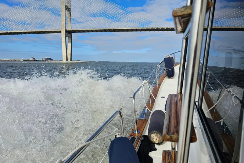 Slide: The Image of Menorquin 120 boat cruising under a bridge, creating waves, 2003 model. - 2