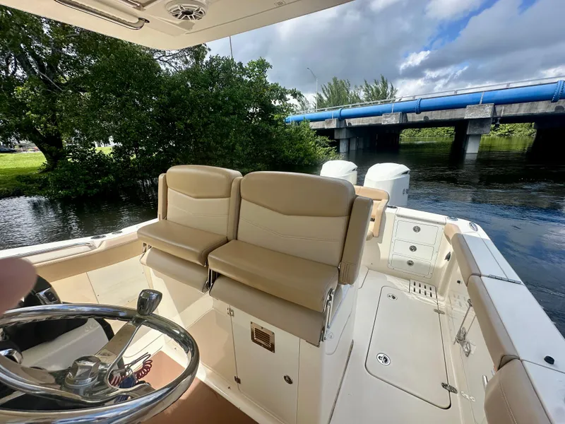Slide: The Image of 2021 Scout 305 LXF boat interior with seating, near a bridge and lush greenery. - 2