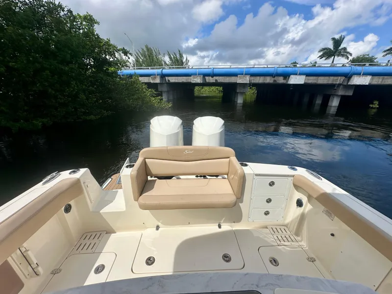 Slide: The Image of 2021 Scout 305 LXF boat interior with seating, near a bridge and lush greenery. - 6