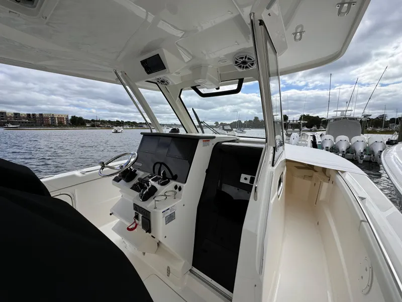 Slide: The Image of 2023 Pursuit S 328 Sport boat interior with steering console, docked by the water. - 13