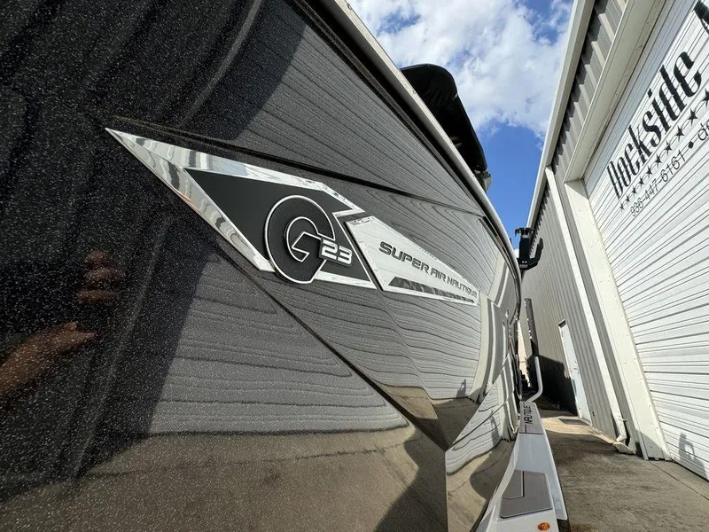 Slide: The Image of 2023 Nautique Super Air Nautique G23 boat exterior with logo, dockside view. - 11