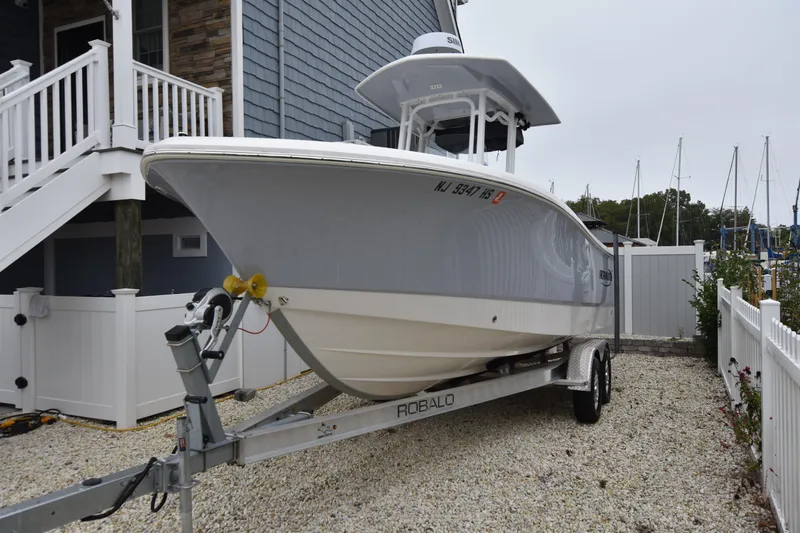Slide: The Image of 2023 Robalo R230 Center Console boat on trailer near a house. - 2