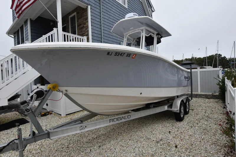 Slide: The Image of 2023 Robalo R230 Center Console boat on trailer, parked beside a house. - 3