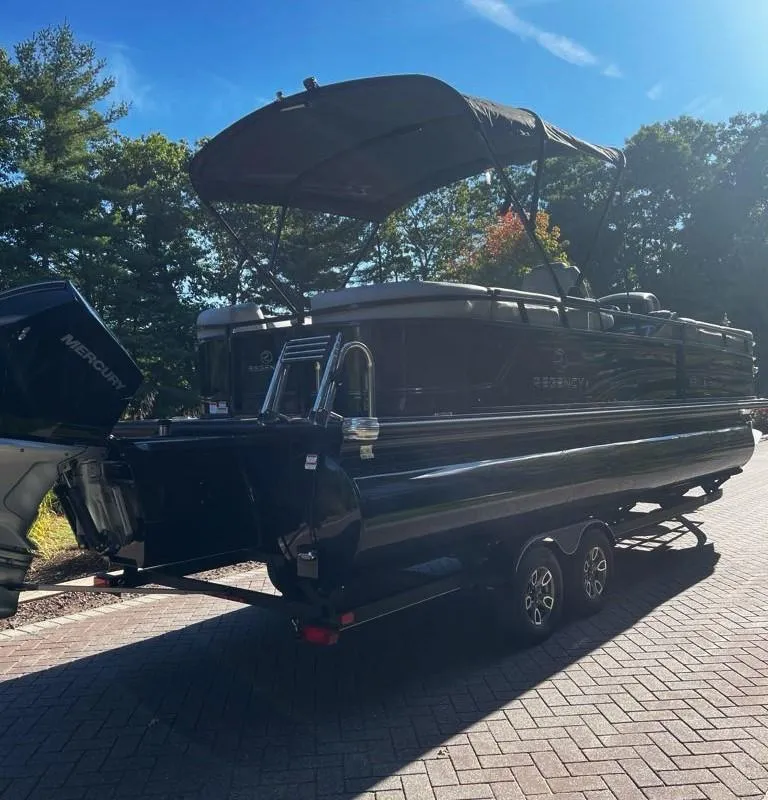 Slide: The Image of 2024 Regency 250 LE3 pontoon boat on trailer, parked outdoors. - 2