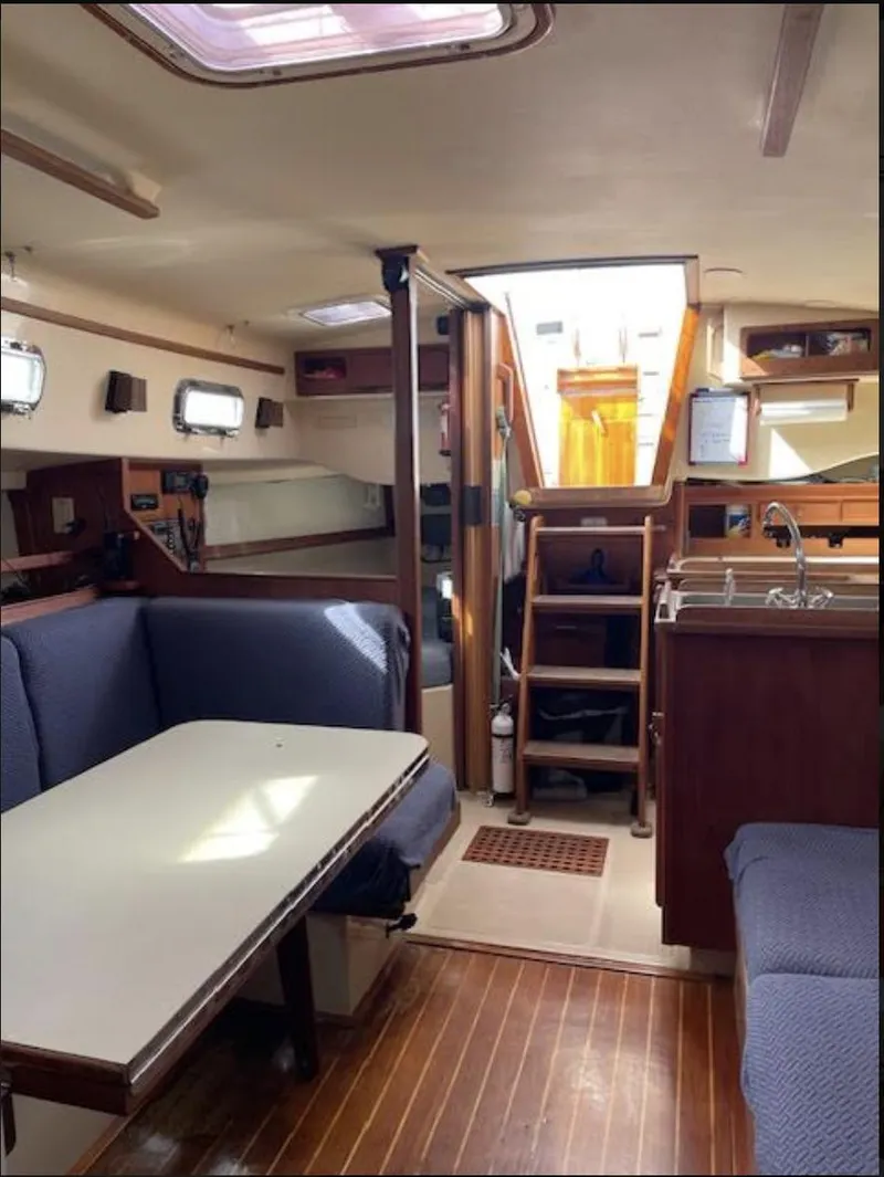 Slide: The Image of 1987 Island Packet 31 sailboat interior with dining area, wooden flooring, and compact kitchen. - 10