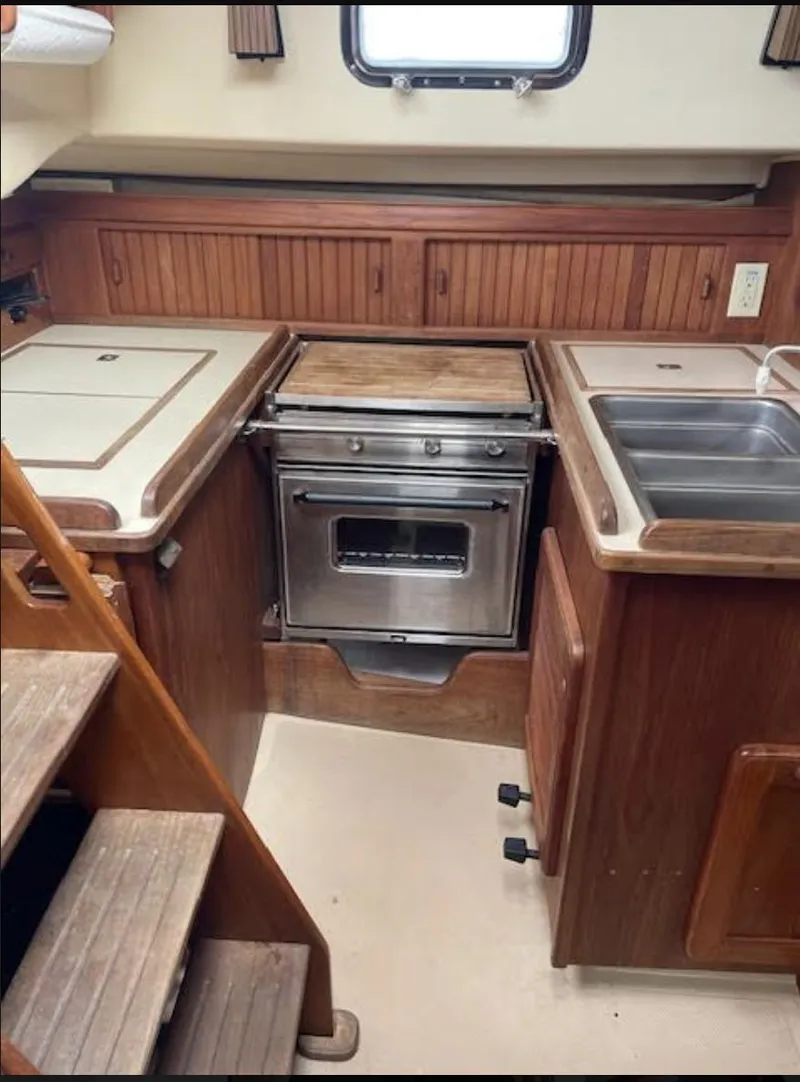 Slide: The Image of 1987 Island Packet 31 yacht kitchen with stove, sink, and wooden cabinetry. - 12