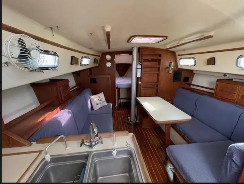 Slide: The Image of Interior of a 1987 Island Packet 31 sailboat, featuring a cozy cabin with seating and a kitchenette. - 7