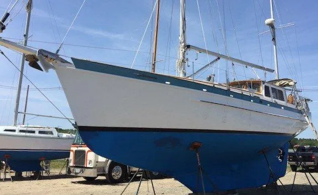 Slide: The Image of 1986 Covey Island 38 sailboat on land, blue and white hull, clear sky background. - 25