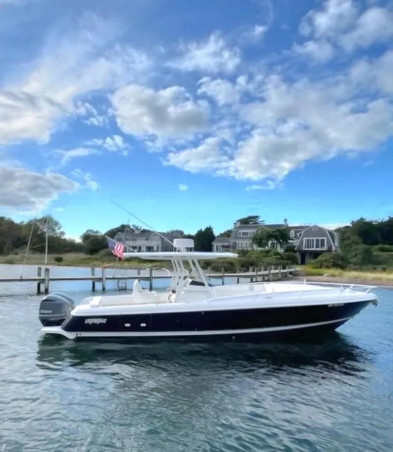 Slide: The Image of 2016 Intrepid 327 Cuddy boat on water, clear sky, waterfront homes in background. - 2