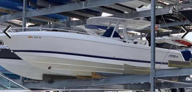 Slide: The Image of 2016 Intrepid 327 Cuddy boat in storage, sleek design, white with blue accents. - 23