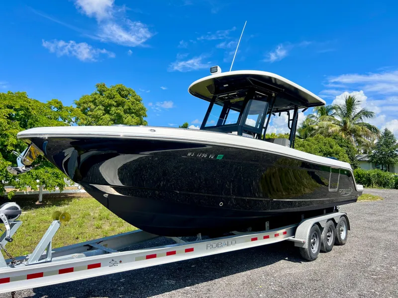 Slide: The Image of 2021 Robalo R272 Center Console boat on trailer, parked outdoors under blue sky. - 2
