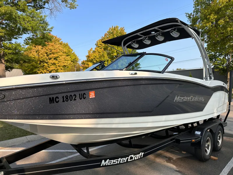 Slide: The Image of 2017 MasterCraft NXT22 boat on trailer, parked outdoors with trees in the background. - 21