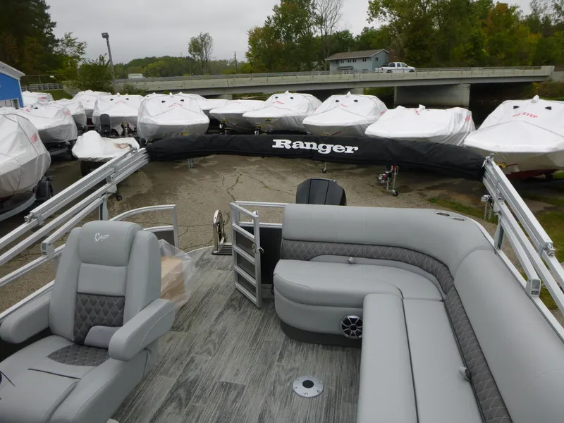 Slide: The Image of 2024 Ranger Reata 223C pontoon boat with gray seating, docked near covered boats. - 22