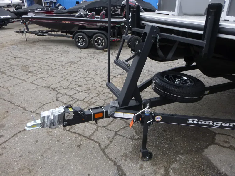 Slide: The Image of 2024 Ranger Reata 223C boat trailer with hitch and spare tire on cracked pavement. - 9