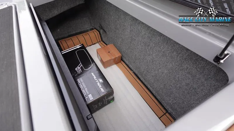 Slide: The Image of 2025 Nautique Super Air Nautique G25 storage compartment with boxes, Race City Marine branding. - 21