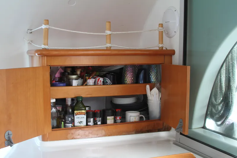 Slide: The Image of Wooden cabinet with open doors, displaying kitchen items on a 2004 Lagoon 380 catamaran. - 33