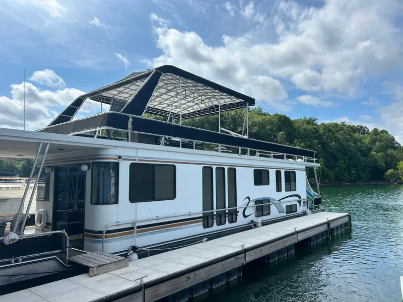 Slide: The Image of 1999 Lakeview houseboat docked on a serene lake under a partly cloudy sky. - 0