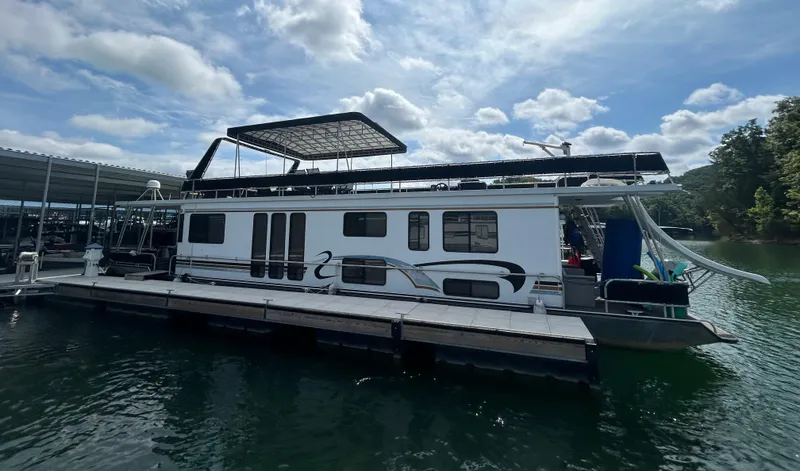 Slide: The Image of 1999 Lakeview houseboat docked on a serene lake under a partly cloudy sky. - 3