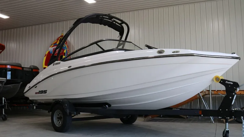 Slide: The Image of 2025 Yamaha AR195 boat in showroom, sleek white design on trailer. - 2