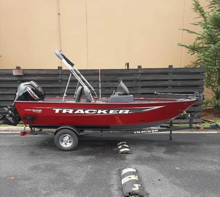 The Image of 2025 Tracker Pro Guide V-16 SC boat on trailer, red exterior, parked outdoors. - 0
