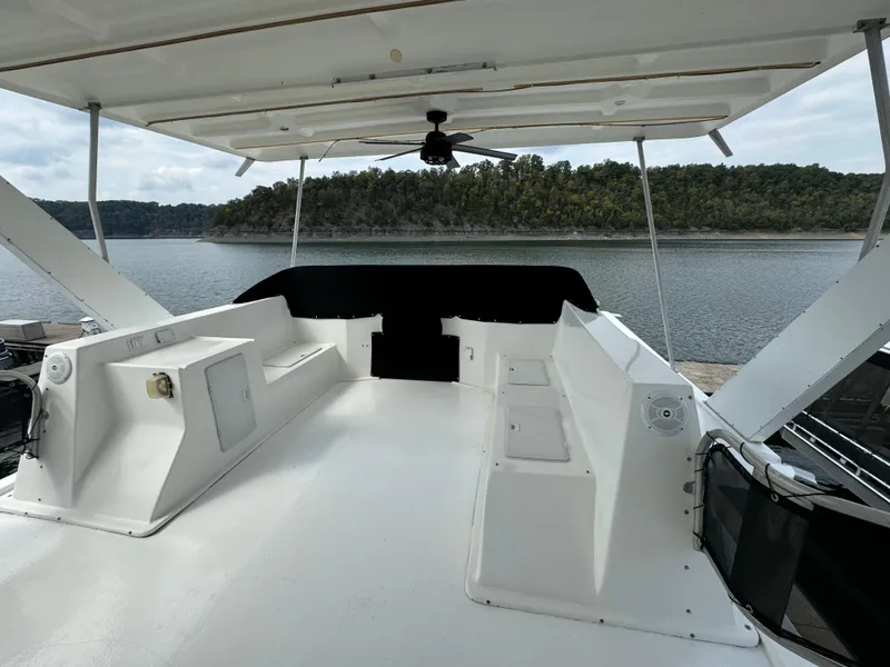 Slide: The Image of 1999 Sumerset 16 X 80 houseboat deck with seating, overlooking a serene lake and forested shoreline. - 7