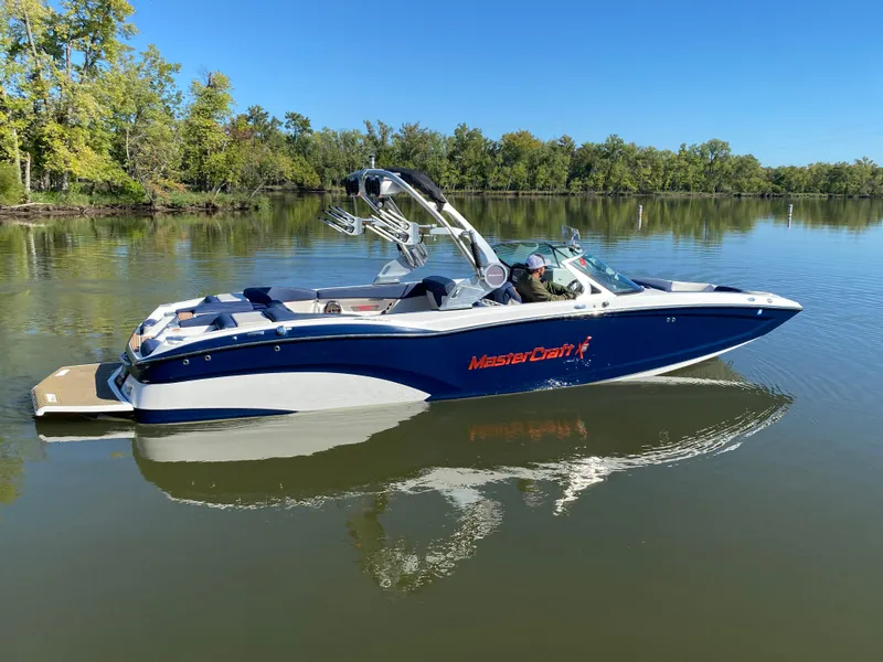 Slide: The Image of 2018 MasterCraft X26 boat on calm lake with lush green trees. - 12