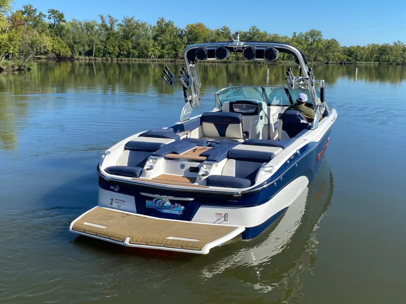 Slide: The Image of 2018 MasterCraft X26 boat on a calm lake, surrounded by trees. - 14