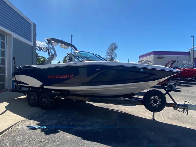 Slide: The Image of 2018 MasterCraft X26 boat on trailer, parked outdoors under clear blue sky. - 2