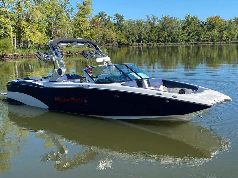 Slide: The Image of 2018 MasterCraft X26 boat on a calm lake with lush green trees. - 7