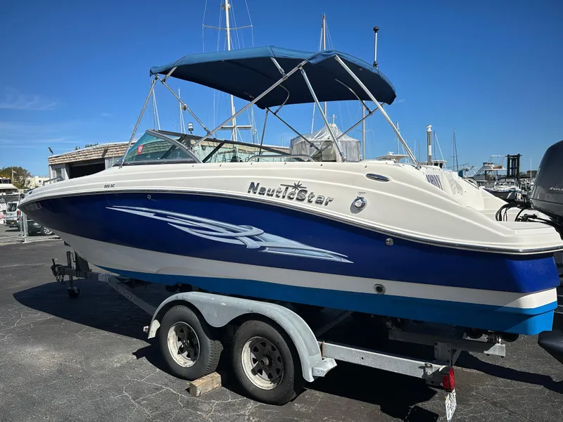 Slide: The Image of 2014 NauticStar 223DC Sport Deck boat on trailer, blue and white design, docked outdoors. - 2