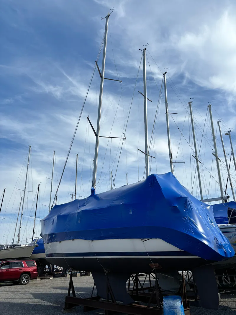 Slide: The Image of 2001 Hunter 320 sailboat covered in blue tarp, stored on land under a cloudy sky. - 11