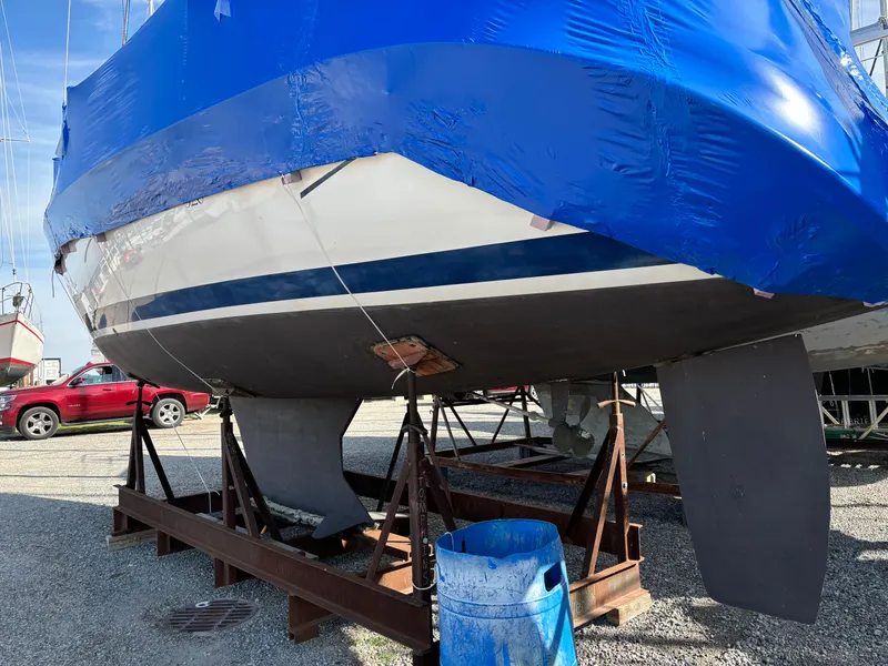 Slide: The Image of 2001 Hunter 320 sailboat on stands, covered in blue tarp, with visible keel and rudder. - 3