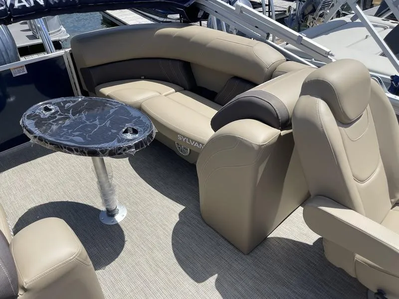 Slide: The Image of 2024 Sylvan Mirage 8524 LZ boat interior with beige seating and a round table. - 13