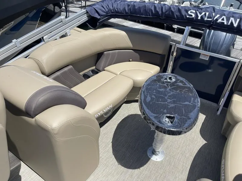 Slide: The Image of 2024 Sylvan Mirage 8524 LZ boat interior with beige seating and round table. - 15