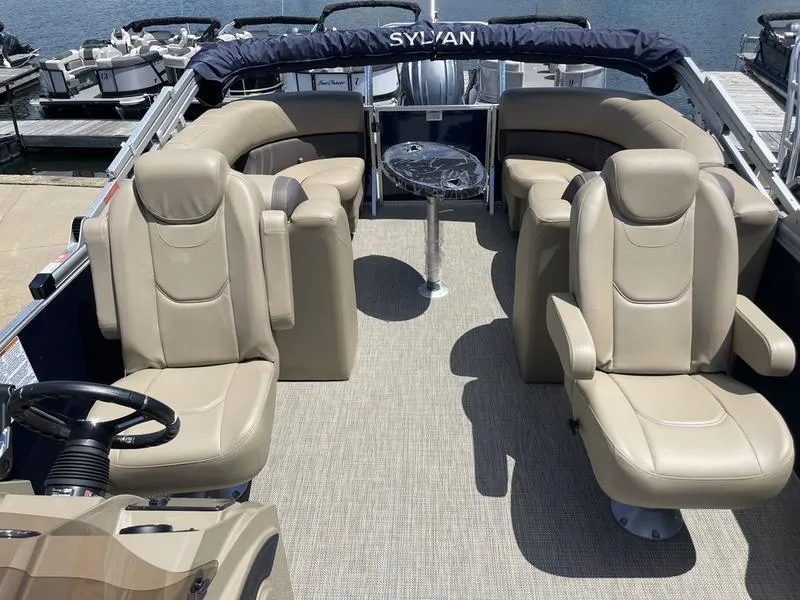 Slide: The Image of 2024 Sylvan Mirage 8524 LZ pontoon boat interior with beige seating and table. - 8