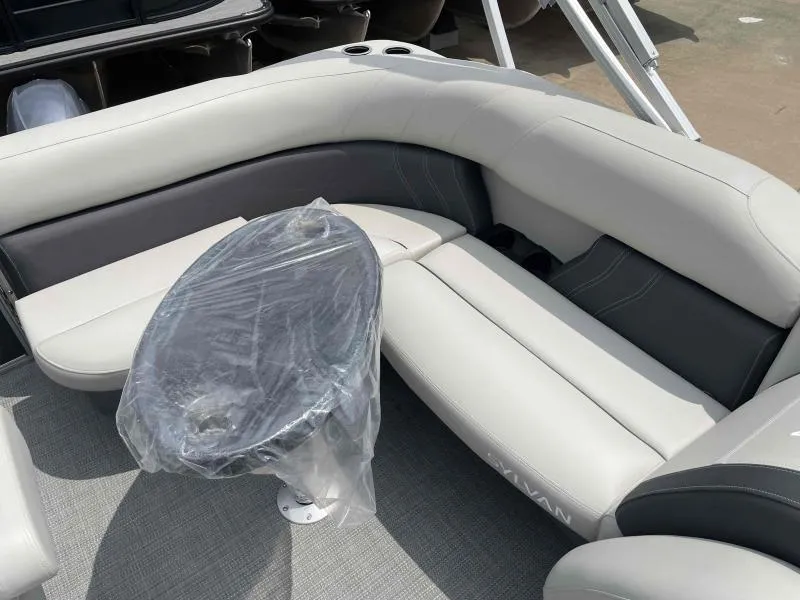 Slide: The Image of 2024 Sylvan Mirage 818 Fish boat interior with cushioned seating and covered table. - 12
