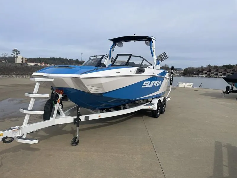 Slide: The Image of 2023 Supra SUPRA SA 450 boat on trailer, blue and white design, dockside view. - 2